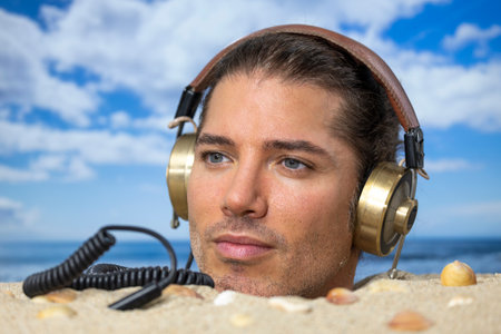Man buried in sand on beach with headphones