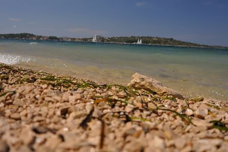 Closeup seashore rock beach with sails and distant seashore