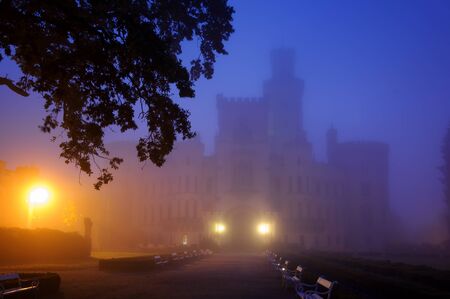 Mysterious castle in fog night. Dark blue sky and few shinning lanternsの写真素材