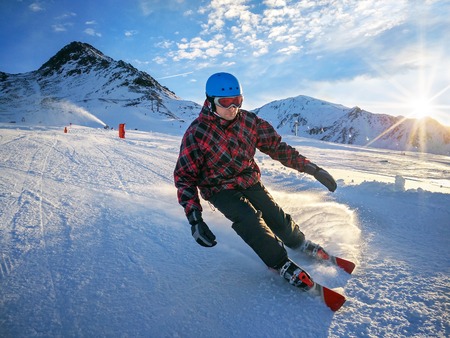Skier on piste in high mountains with beautiful sky on sunny day. Active downhill ride.