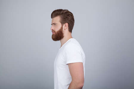 Profile shot of handsome male with trendy hairdo and beard, looks aside with serious expression, has thick red beard, isolated over white backgroundの写真素材