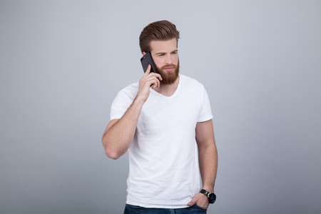 Serious handsome bearded man talking on cell phone over white backgroundの写真素材