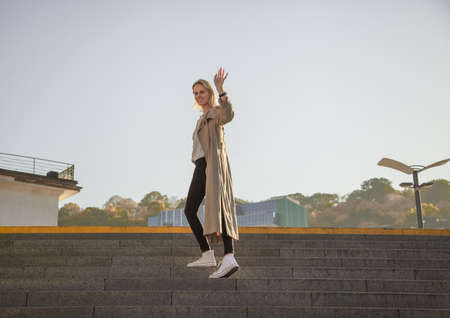 Young woman in a stylish spring coat in fashionable glasses in a white T-shirt in a black leather handbag walking along the street against the background of vintage buildings. European girl.の写真素材