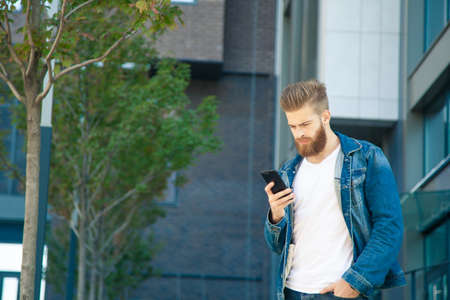 Portrait of young hipster man reading message on the street.の写真素材