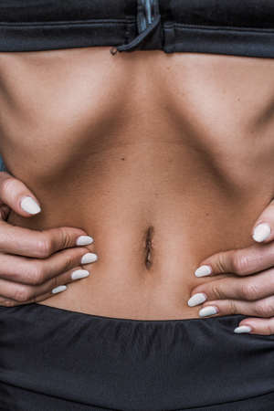 Vacuum belly close up. A swarthy girl in a sports uniform with a slender body pulls in her stomachの写真素材