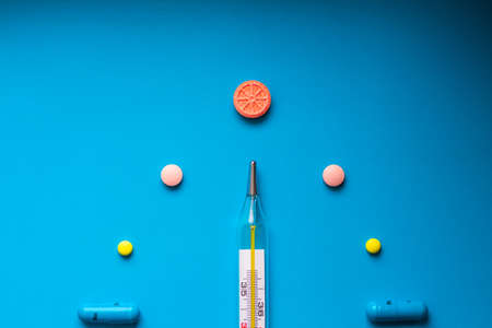 A mercury thermometer for measuring body temperature, surrounded by multi-colored tablets and...