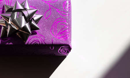 Beautiful sparkling gift box of purple color with the image of roses with a silver bow on top on a white backgroundの写真素材