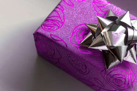 Beautiful sparkling gift box of purple color with the image of roses with a silver bow on top on a white backgroundの写真素材