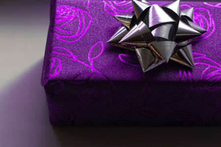 Beautiful sparkling gift box of purple color with the image of roses with a silver bow on top on a white backgroundの写真素材