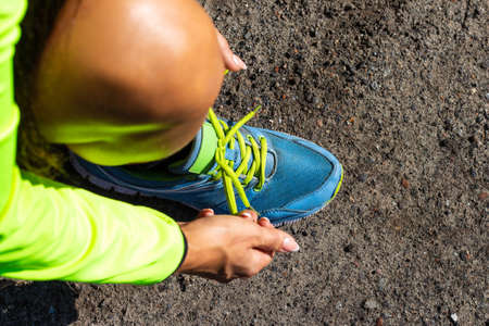 A girl in bright sportswear and blue sneakers ties her shoelaces before a morning jogの写真素材
