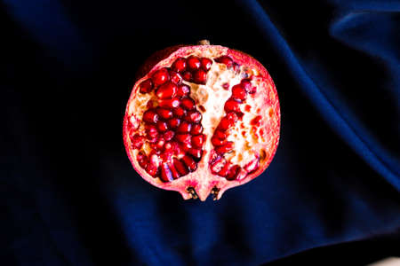 Half a pomegranate on a dark fabric background. Deep red saturated pomegranate fruit on black and blue silk fabricの写真素材