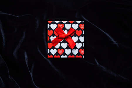 Gift box with the image of red hearts for valentines day on a black velvet background. Valentines...