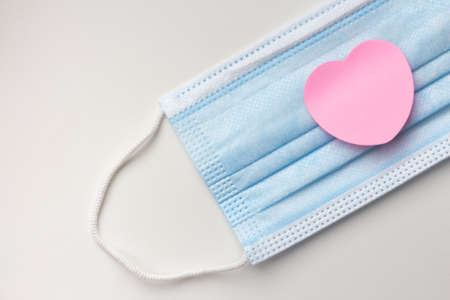 Pink sticker in the shape of a heart on a blue protective medical mask. Mask for protection against on a light background. Valentines Day in quarantine.の写真素材