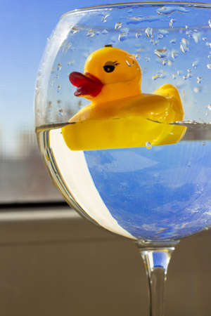 Rubber yellow duck with big red lips swims in a large glass of water against a blue sky. Vacation and travel concept. Ukraine flag colorsの写真素材