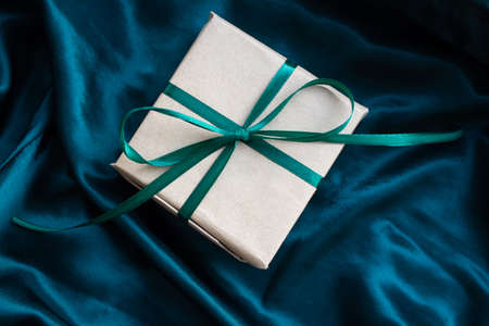 Gift box wrapped in craft paper with emerald green satin ribbon. Happy New Year. Birthday present on silk emerald green backgroundの写真素材