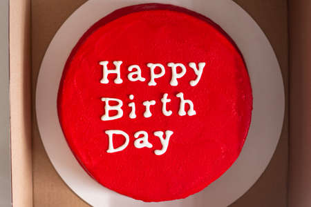 Birthday cake with lettering on top isolated on red. Red round birthday cake with an inscription wishing happy birthday in a boxの素材 [FY310187968389]