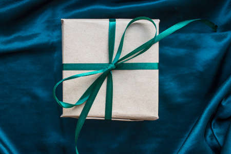 Gift box wrapped in craft paper with emerald green satin ribbon. Happy New Year. Birthday present on silk emerald green backgroundの写真素材