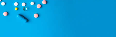 Medical banner with place for text. Pills and capsules of different colors on a blue background. The concept of medicine and health. Copy spaceの写真素材