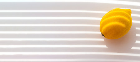 Whole ripe yellow lemon on a white background with shadow from the blinds. Food concept. Tropical organic fruits, citrus, vitamin C. Summer minimalistic fruit background. Banner with place for textの写真素材