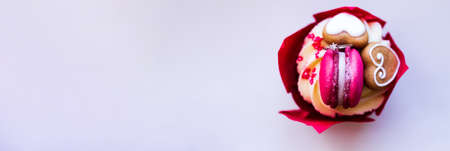 Appetizing red cupcake with a diamond ring inside for a marriage proposal on a light background. Banner with place for text. Sweet holiday dessert with cream, gingerbread and macaroons.の写真素材