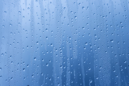 Close-up of raindrops on a window pane. Gloomy wet weather. Drops of water on glass in front of dark blue rain clouds. Rain. Abstract background texture. Wallpaper.の写真素材