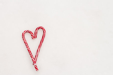 Festive minimalistic white background. A heart of sweet red striped candies on a background of white snow. Love. Valentine. Creative gift ideas for Valentine's Day. The 14th of February. Photo with a place for an inscription, top view. High quality photoの写真素材
