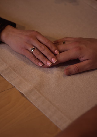 Newlyweds hands with wedding rings. A young married couple hold hands in a restaurant during a romantic dinner. Valentines Day. Romance and love. Close-up of a pair of hands on a restaurant tableの写真素材