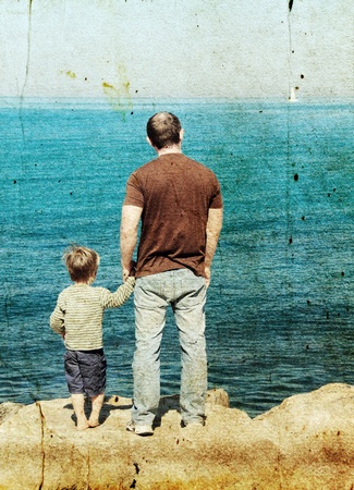 Father and son looking at a white sail in the sea. Photo in old image style.の写真素材