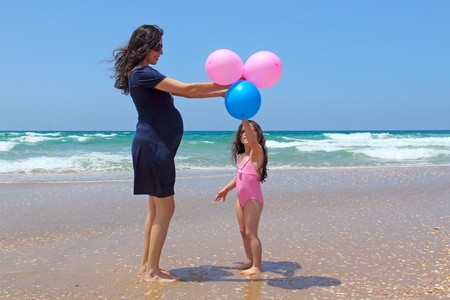 Pregnant mother with daughter on the beach with balloonsの写真素材