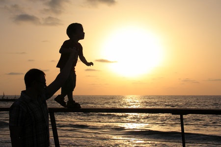 silhouettes of father and son on sunset sea background の写真素材