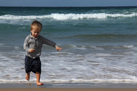 3-year-old child running away from the waves  Autumn sea, strong waves, sharp colors の写真素材