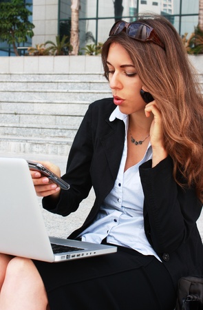 Young businesswoman with two mobile phones and laptopの写真素材