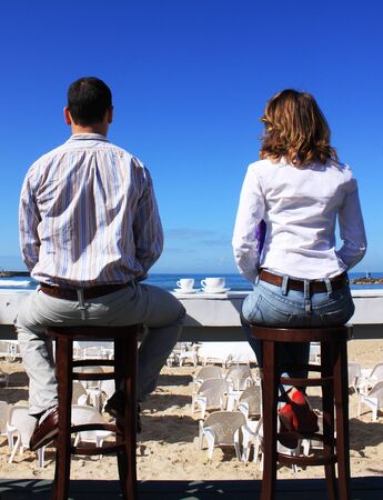 Girl and boy drinking coffee and watching the seaの写真素材