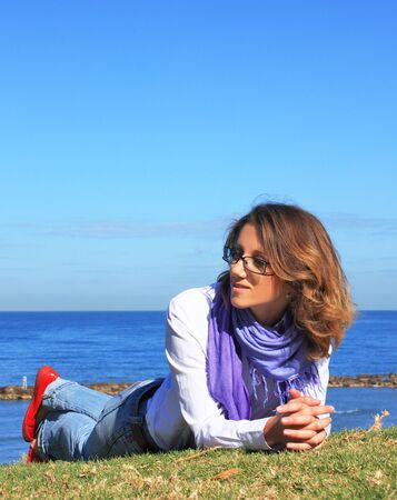 Girl lying on the grass, in the background of blue sea and blue sky の写真素材