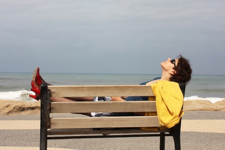 Beautiful young girl resting on a bench next to the seaの写真素材