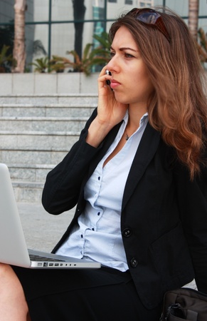 Business woman sitting on stairs with laptop and talking on the phoneの写真素材
