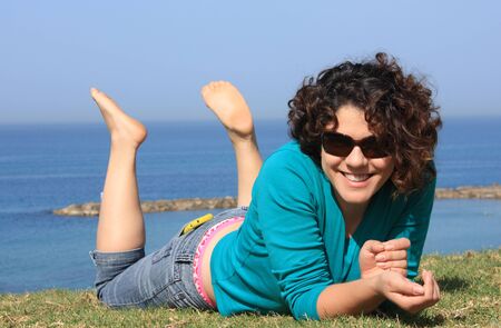 Girl lying on the grass and smiling  In the background of blue sea and blue sky の写真素材