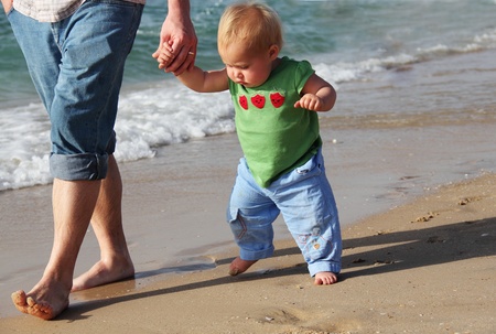 child taking her first steps. Father and daughter of the sea.の写真素材