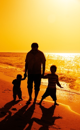 Father and two kids silhouettes on the beach at sunsetの写真素材