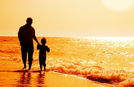 silhouettes of father and son on sunset sea backgroundの写真素材