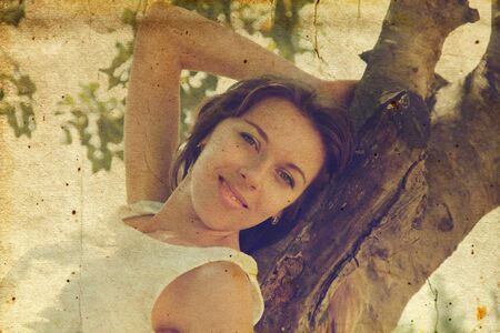 Beautiful girl in white dress sitting on the tree  Photo in old image style の写真素材