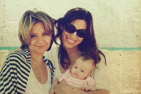 two beautiful girls with a baby on the beach in old color image style.の写真素材