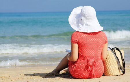 young girl in white hat and red dress on the beachの写真素材