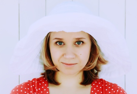 girl in red dress and white hat against a white wooden fenceの写真素材