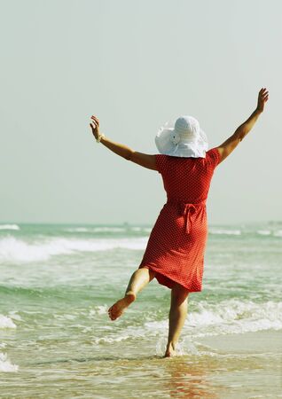 young girl in white hat and red dress on the beachの写真素材