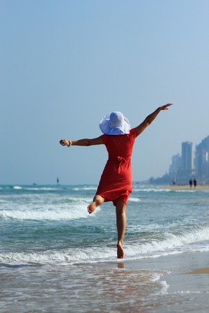 young girl in white hat and red dress on the beachの写真素材