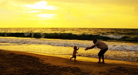 father and daughter playing together on the beach at sunsetの写真素材