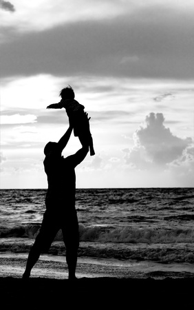 father and daughter playing together on the beach at sunsetの写真素材
