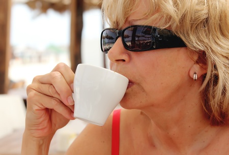 Portrait ofattractive woman with cup of hot drink (coffee or tea) at the beachの写真素材