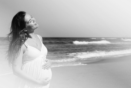 beautiful pregnant woman standing on the beachの写真素材